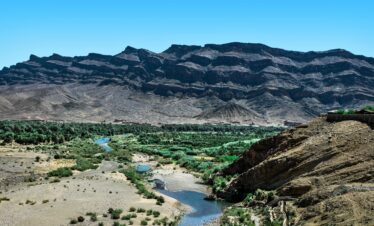 Stunning view of the rugged mountains and lush valley in Zagora, Morocco, under a clear blue sky.