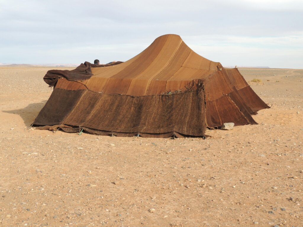 Brown nomadic tent set in a barren desert landscape under a clear sky.
