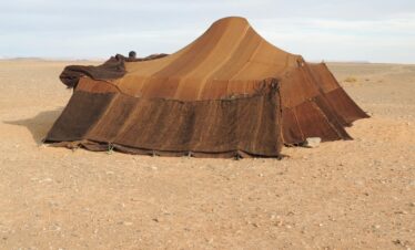 Brown nomadic tent set in a barren desert landscape under a clear sky.