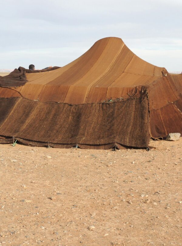Brown nomadic tent set in a barren desert landscape under a clear sky.