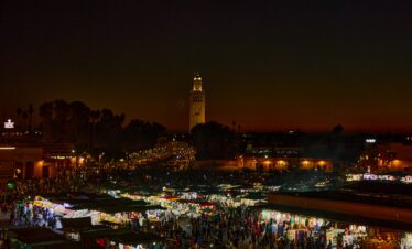 Experience the bustling night market in Marrakesh, Morocco, illuminated against a stunning twilight sky.
