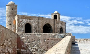 Explore the historic fortress walls of Essaouira, Morocco, against a vibrant blue sky.