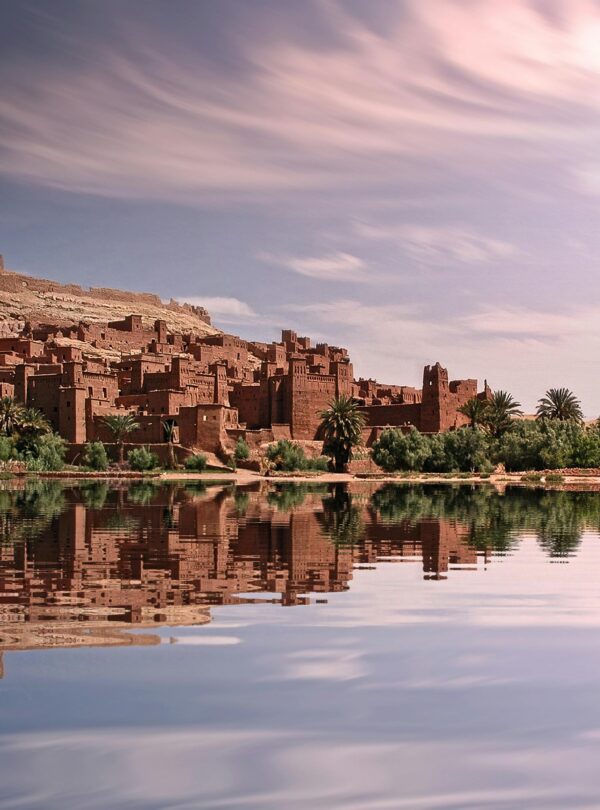 Picturesque reflection of Ouarzazate's historic ksar by the river under a vibrant sky.