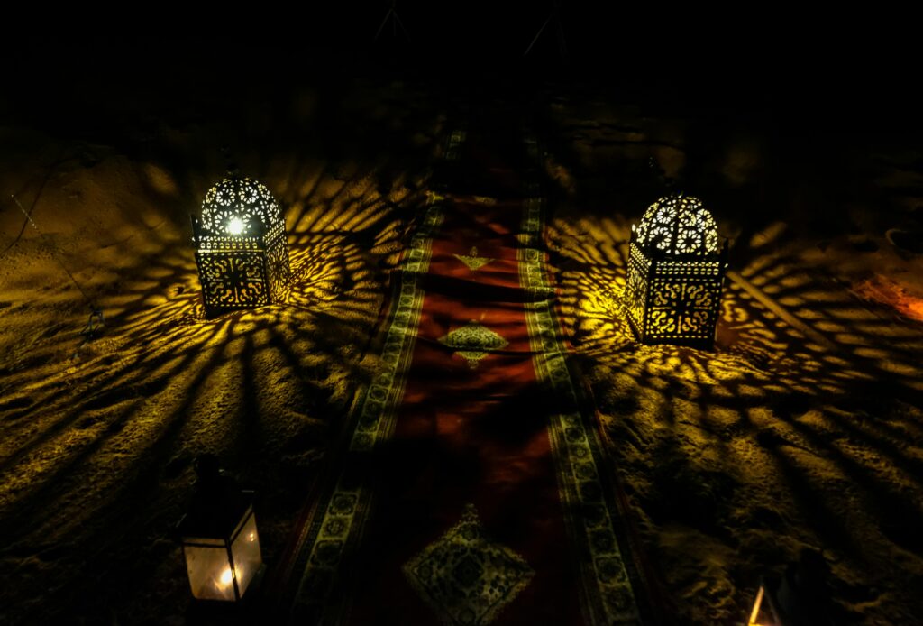 Decorative Moroccan lanterns casting intricate light patterns on sand at night.