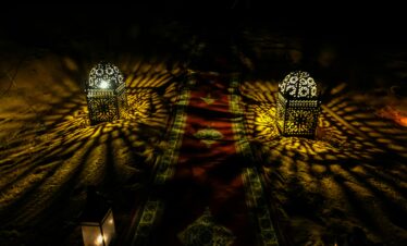 Decorative Moroccan lanterns casting intricate light patterns on sand at night.
