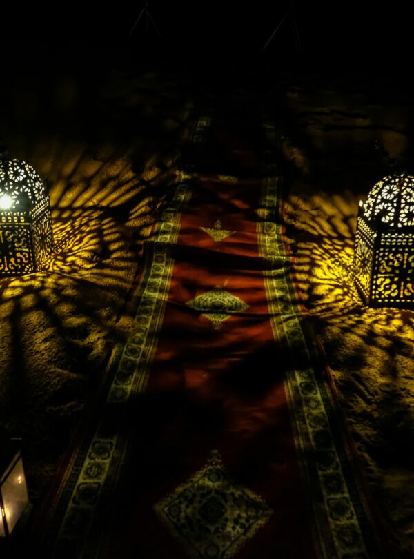 Decorative Moroccan lanterns casting intricate light patterns on sand at night.